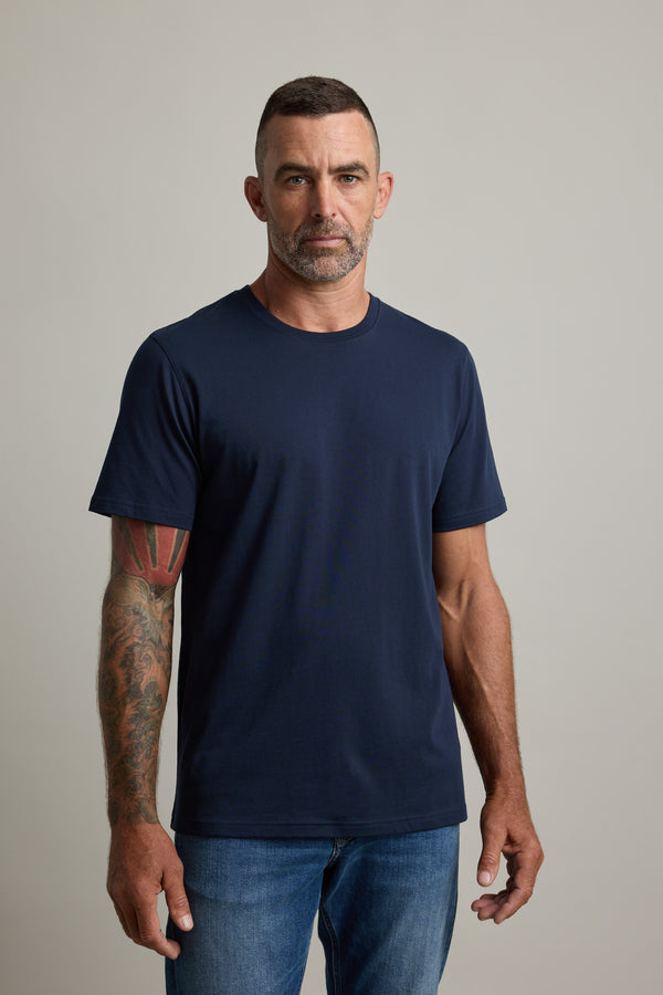 Tattooed man wears Barkers Good Earth Cotton Essential Tee and jeans, against plain background.