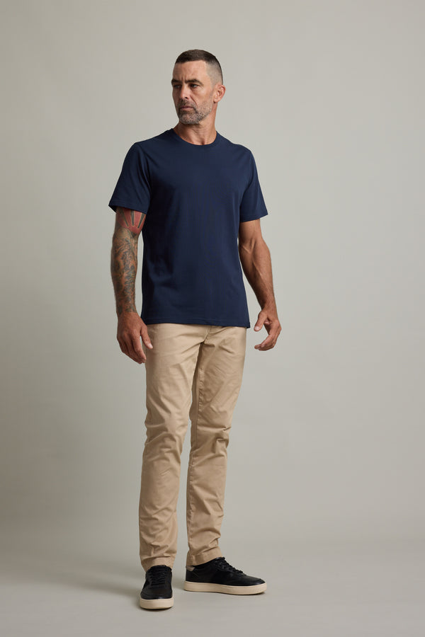 Man in Barkers Good Earth Cotton Essential Tee and beige pants stands against plain backdrop.