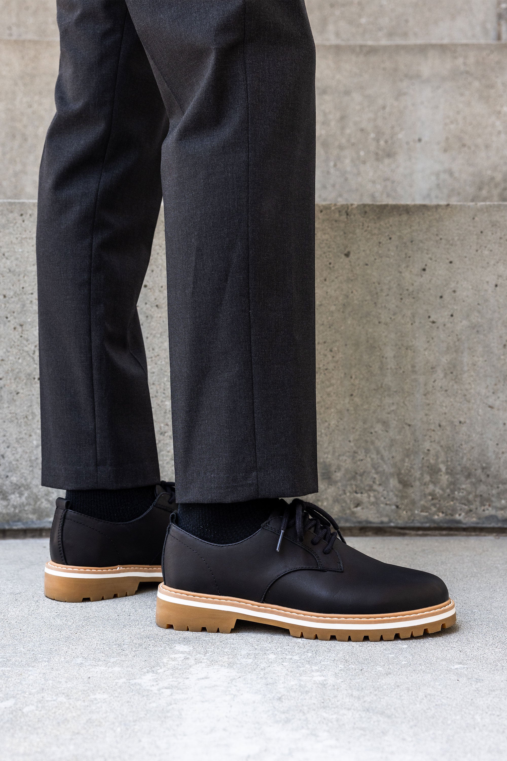 Person wearing Clae Logan shoes with premium leather and tan soles on concrete steps.