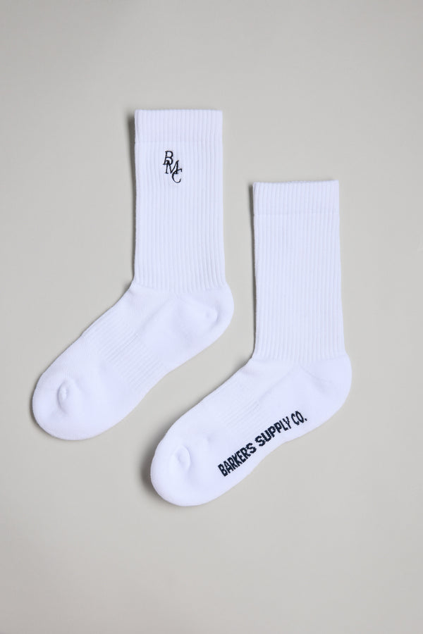 Two white Barkers BMC Ribbed Socks are shown on a light gray background; one features "BMC" embroidered near the top, while the other displays "BANKERS SUPPLY CO." printed on the foot.