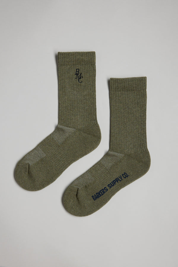 A pair of olive green BMC Ribbed Socks by Barkers, featuring "RMC" embroidery near the top of one sock and "BANKERS SUPPLY CO." in black on the sole of the other, laid flat on a light background.