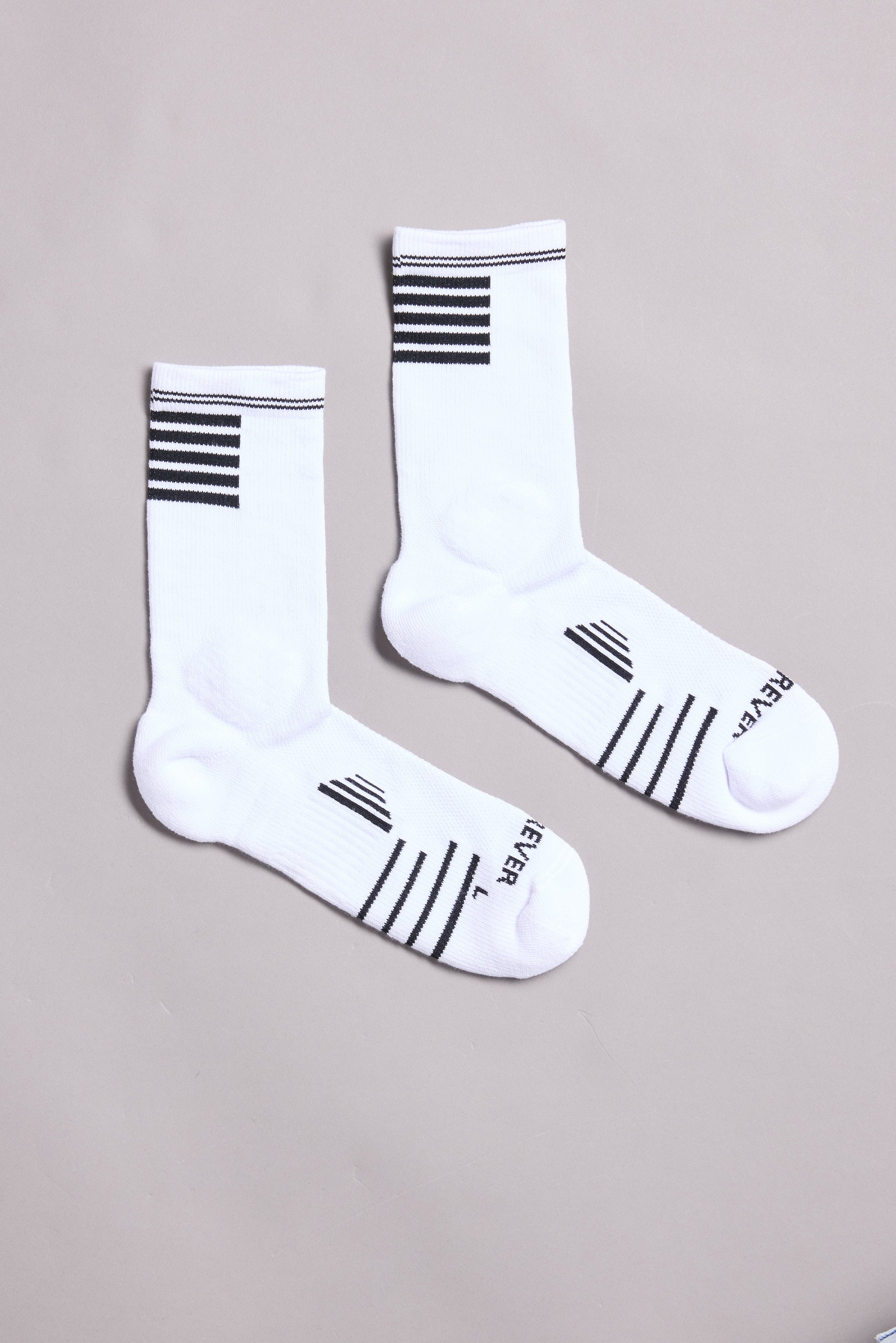 A pair of WearEver Active Socks by WearEver in white crew style, featuring black stripes near the cuffs and toes and "REVER" and "LEVEL" printed on the soles, displayed on a light gray background.