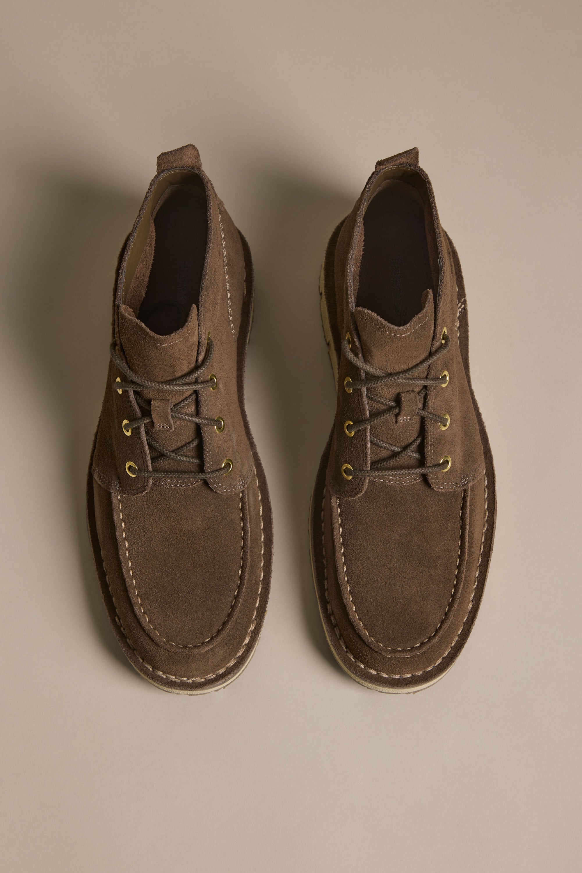 Timberland Westmore Chukka boots in brown suede with white stitching, top view on neutral background.