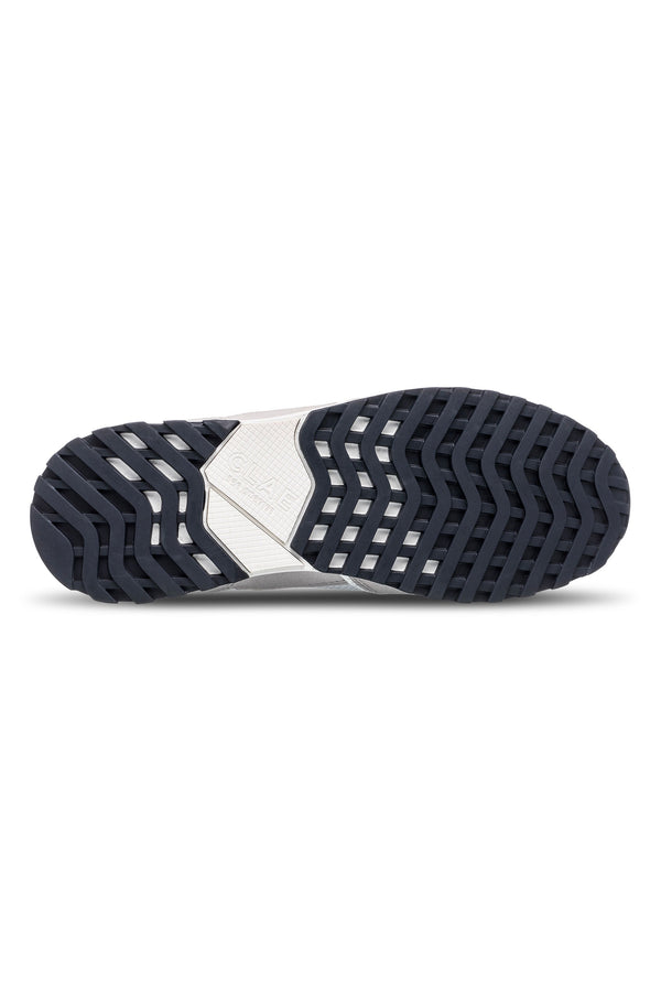 The image shows the bottom view of the Clae - Joshua sneaker, featuring a black textured rubber sole with a zigzag grip and a central white section made from recycled materials.