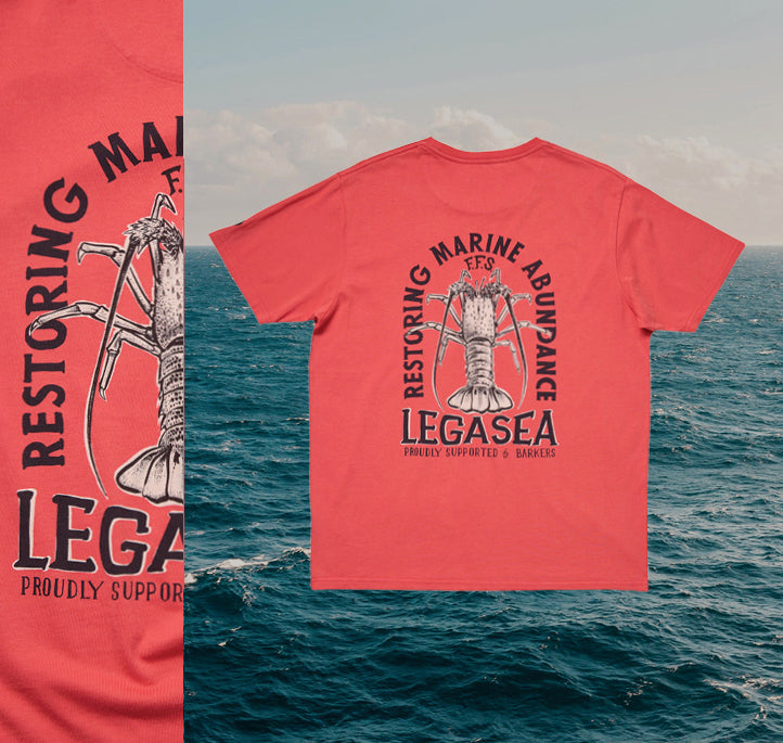 A coral-colored t-shirt with a large lobster graphic and the text Restoring Marine Abundance, Legasea, and Proudly Supported by Barkers printed on the back, displayed over an ocean background.