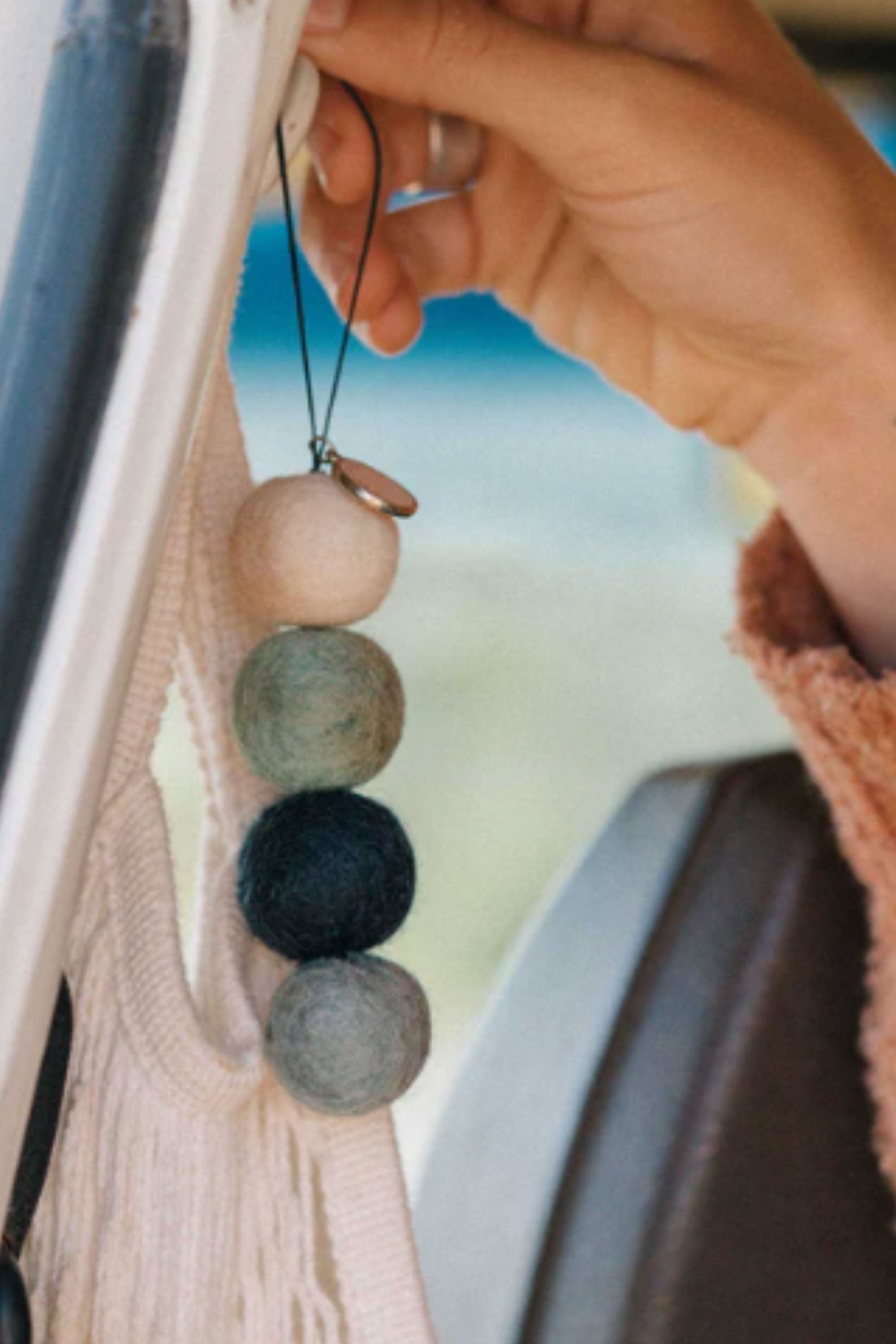 A hand hangs Smelly Balls: Cove / Coastal Drift air freshener by Other in a vehicle.